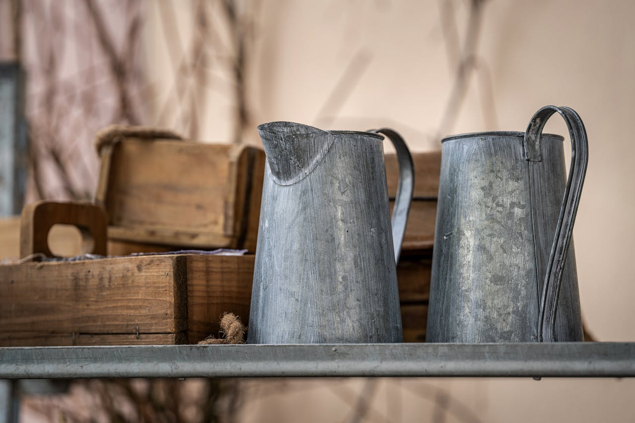 Vintage metal pitchers and wooden boxes on a rustic shelf, evoking farmhouse charm.